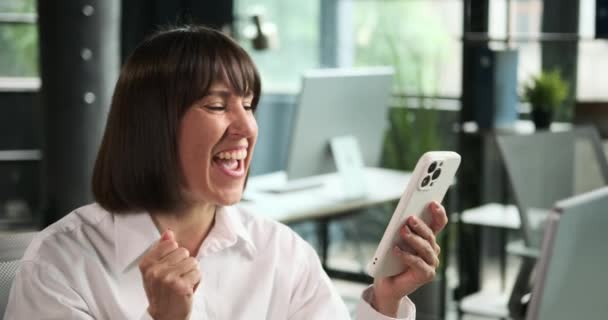 Радостная белая женщина-менеджер празднует захватывающие новости по телефону. Ее восторженное выражение лица и положительная реакция отражают счастье, принесенное новостью, которую она получила. - Кадры, видео