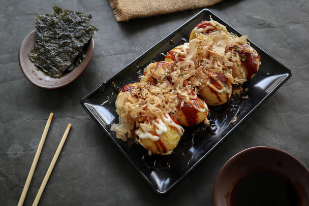 Takoyaki ist ein japanisches Gericht aus Weizenmehlteig, Krakenfleisch oder anderen Füllungen, das mit Sauce, Mayonnaise und Topping in Form von Katsuobushi oder Holzfischspänen serviert wird.. - Foto, Bild
