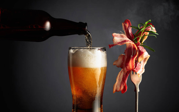 Beer and slices of tasty fried bacon garnished with rosemary. Copy space. - Фото, изображение