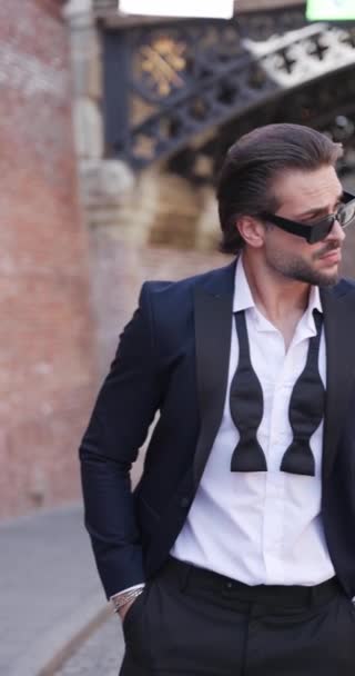 atractivo hombre elegante con gafas de sol cogidas de la mano en los bolsillos, mirando a un lado y ajustando traje y pensando - Metraje, vídeo