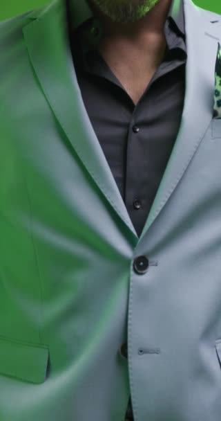 Nahaufnahme Video von eleganten Mann mit offenem Kragen Hemd hält die Hände in der Tasche, schaut zur Seite und posiert auf grauem Hintergrund mit bunten Lichtern auf - Filmmaterial, Video
