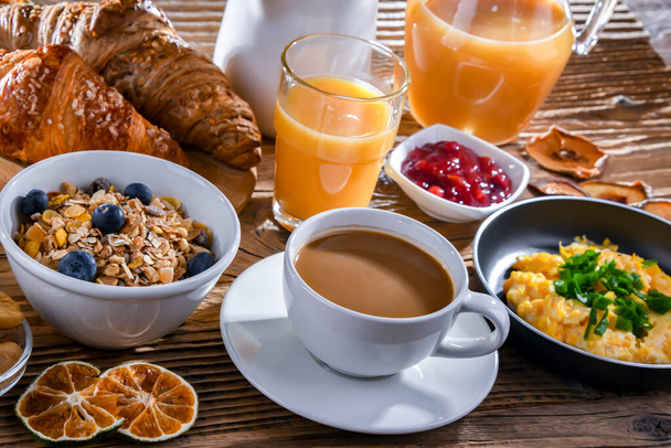 Πρωινό σερβίρεται με καφέ, χυμό πορτοκαλιού, ομελέτα, δημητριακά, τηγανίτες και κρουασάν. - Φωτογραφία, εικόνα