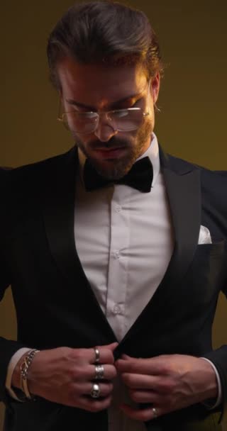 close up video of elegant young man unbuttoning and adjusting tuxedo and glasses, looking to side and being confident on colorful background - Footage, Video