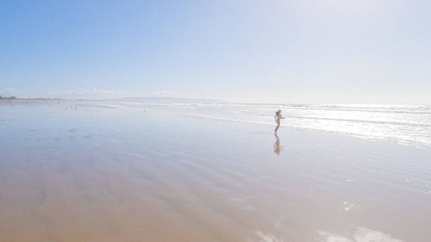 Little girl, braving the cold, joyfully runs in her swimsuit across the beach during winter. - Photo, Image