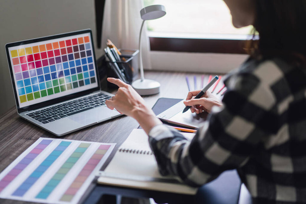 Γυναίκα σχεδιαστής καλλιτέχνης επιλέγοντας δείγματα χρώμα Swatch στο laptop και το λογότυπο σχεδίασης σε tablet γραφικών. - Φωτογραφία, εικόνα