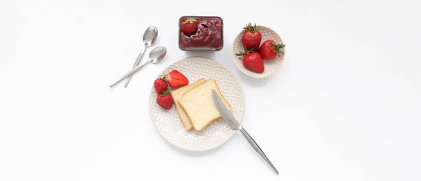 Teller mit leckerem Brot und süßer Erdbeermarmelade auf weißem Hintergrund - Foto, Bild