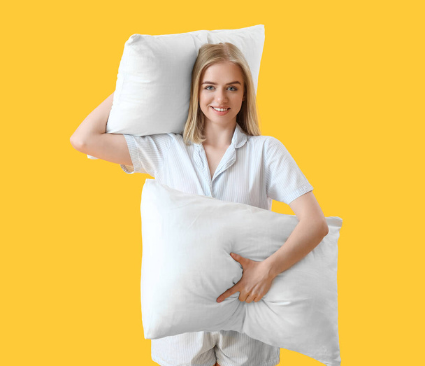 Счастливая молодая женщина в пижаме и с подушками на желтом фоне - Фото, изображение