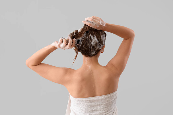 Young woman washing hair on light background, back view - Valokuva, kuva
