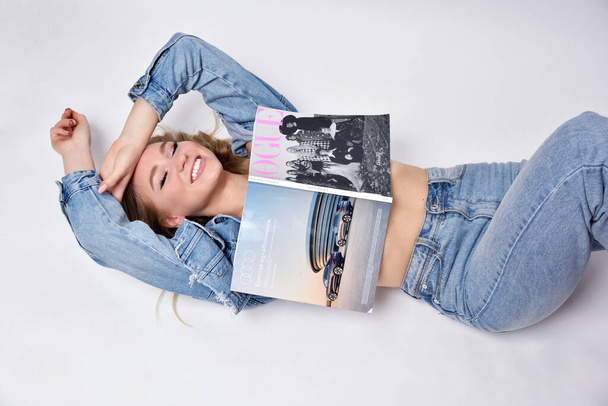 WROCLAW, POLEN - MEI 18: Jonge vrouw met Vogue magazine. Charmant blond model met jeans jas en broek. - Foto, afbeelding