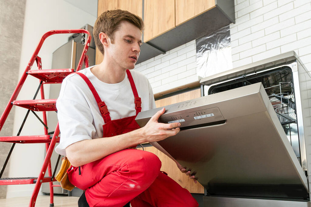 Repairman checks operating state of dishwasher in kitchen. - Photo, Image