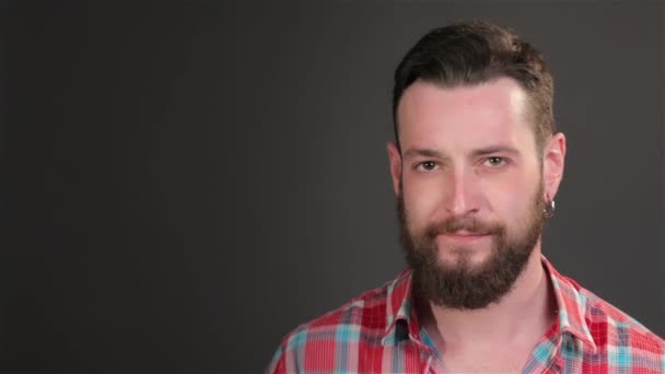 Close up of young bearded man showing dissappointment. Caucasian guy covering his eyes by his hand. Brunette hipster dressed in checkered shirt isolated on dark gray background - Footage, Video