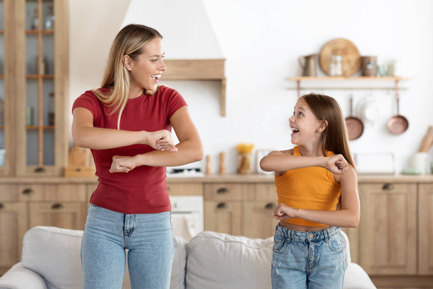 Positive attractive blonde millennial woman mother and cute girl teenager daughter having fun dancing at home, moving their arms bodies, looking at each other and smiling, enjoying time together - Foto, imagen