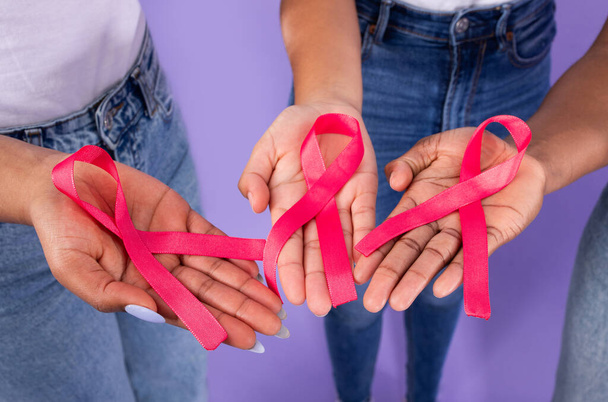 Świadomość o raku piersi. Przycięte ujęcie grupy czarnych pań trzymających różowe wstążki, zbliżenie dłoni z symbolami onkologii na fioletowym tle studia. Widok z góry - Zdjęcie, obraz