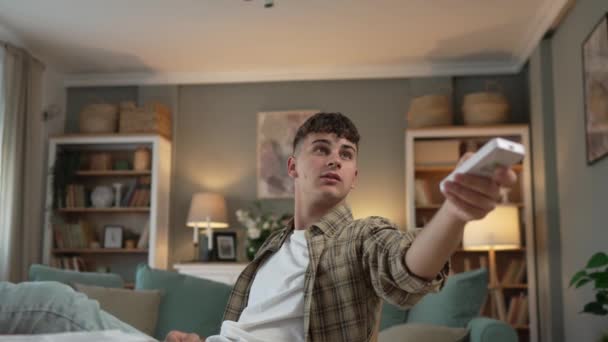 Nuori valkoihoinen teini-ikäinen mies käyttää kaukosäädintä televisioon tai ilmastointiin hidastettuna - Materiaali, video