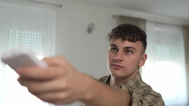Jovem caucasiano adolescente usa controle remoto para TV ou ar-condicionado câmera lenta - Filmagem, Vídeo