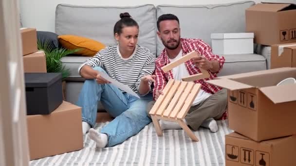 szczęśliwa Młoda para, otoczona pudełkami w nowym mieszkaniu zaangażowana w łatwą budowę nowoczesnego drewnianego montażu mebli półkowych, przenosząc nową dekorację wnętrz - Materiał filmowy, wideo