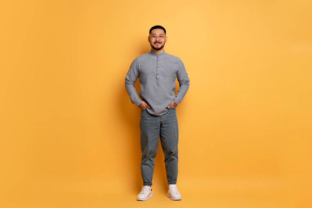 Smiling Young Asian Man Wearing Stylish Eyeglasses Posing Over Blue Studio Background, Handsome Millennial Guy Keeping Hands In Pockets And Looking At Camera, Full Length Shot With Copy Space - Photo, Image