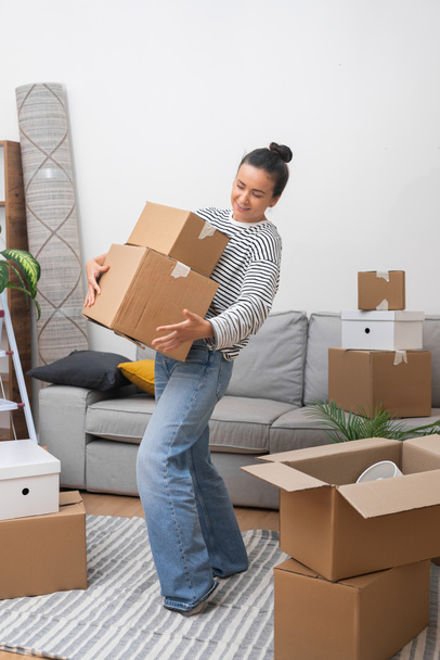 Welkom Thuis: Een gelukkige vrouw, verhuizen naar haar nieuwe huis, komt de woonkamer binnen met een stapel kartonnen verhuisdozen, verwelkomen het gevoel erbij te horen - Foto, afbeelding