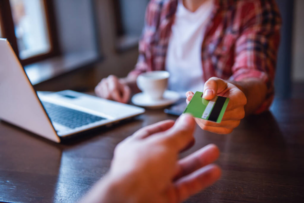 Un bel homme donne une carte de crédit et sourit tout en travaillant avec un ordinateur portable dans un café
 - Photo, image