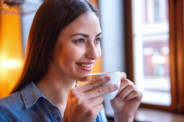 Gyönyörű lány kávét iszik, és mosolyogva, miközben ül a kávézóban - Fotó, kép