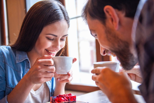 Szczęśliwa para młoda jest picie kawy i uśmiechając się siedząc w kawiarni - Zdjęcie, obraz