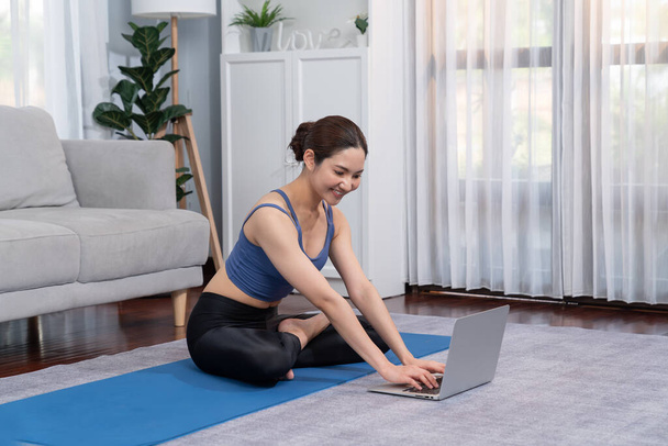 Азіатська жінка в спортивному одязі займається вправами йоги на фітнес-маті, як її домашня тренування тренування рутини. Здоровий спосіб життя жінка дивиться онлайн-відео йоги на ноутбук. Яскравий - Фото, зображення