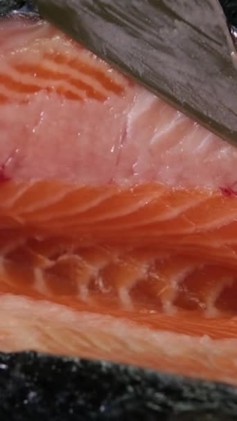 Handen koks close-up. chef snijdt met een mes een rode vis, gerookte zalm op een houten snijplank. Zwart houten tafel op achtergrond. - Video
