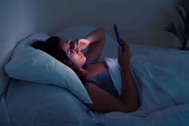 Nuits agitées, prises au piège par les écrans : Une jeune femme, illuminée par ses téléphones brille, lutte contre l'insomnie et les embrayages des médias sociaux  - Photo, image