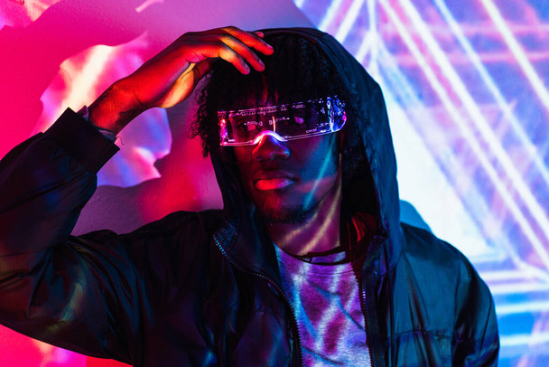 Retrato de estudio con luces de neón púrpura y azul de un hombre futurista fresco con gafas de inteligencia artificial - Foto, Imagen