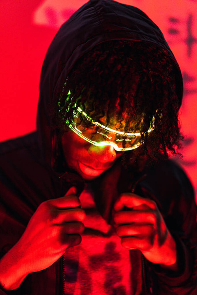 Studio portrait with red neon lights of a cool futuristic afro man with smart glasses - Foto, Imagem