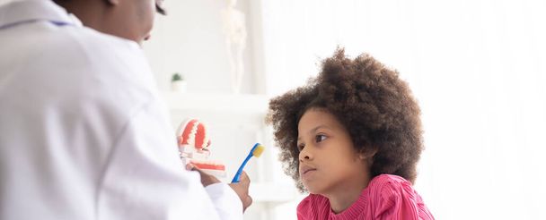 African American dentist explaining to mixed-race afro child how to brush teeth. The doctor and healthcare concept for children. - Photo, Image