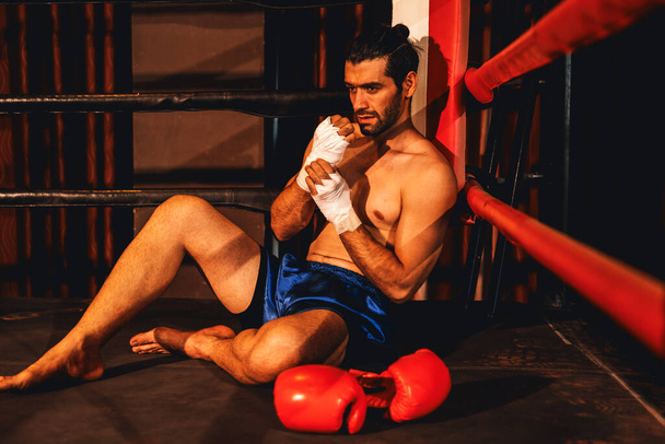 Caucasian boxer with pain and injury after intense boxing training or fighting match, sitting at the edge of ring. Physical injury in sport concept. Impetus - Photo, Image
