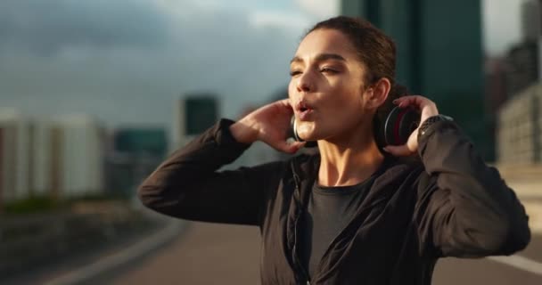 Headphones, calm and woman athlete in city for race, marathon or competition training. Breathe, sports and young female runner listen to music or podcast on break for running cardio workout in town - Footage, Video