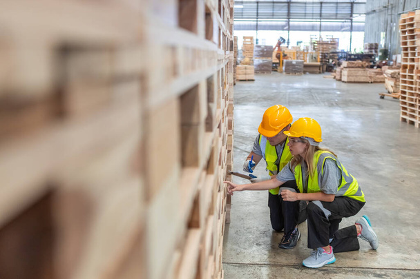 チーム エンジニアの大工は安全制服を身に着け,研修会の製造業の木プロダクトの質を点検するクリップボードを握る堅い帽子を働かせます. 男女労働者 木材倉庫産業. - 写真・画像