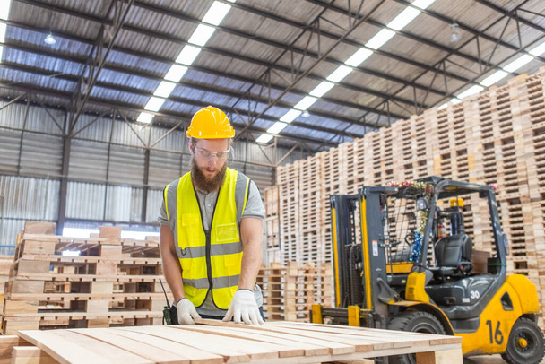 Muž inženýr tesař nosí bezpečnostní uniformu a tvrdý klobouk pracovní kontrolu kvality dřevěných výrobků v dílně výroby. man and woman worker wood warehouse industry. - Fotografie, Obrázek