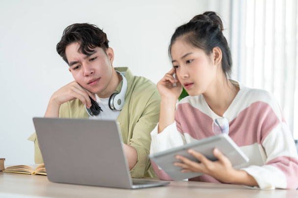 Két összezavarodott és figyelmes fiatal ázsiai főiskolai barátok nézi a laptop képernyőn egy komoly arc, és nem értem az online leckét, miközben együtt tanulnak. - Fotó, kép