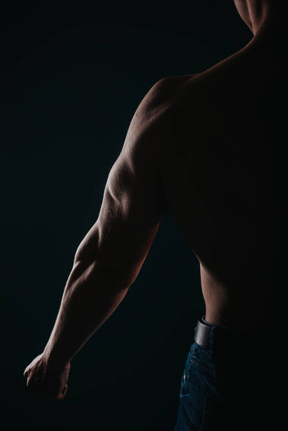 Vahva, hyväkuntoinen, miespuolinen urheilija, joka näyttää tricepsinsä vasemmassa käsivarressaan. Harjoitusmotivaation käsite. Siluettikuva - Valokuva, kuva