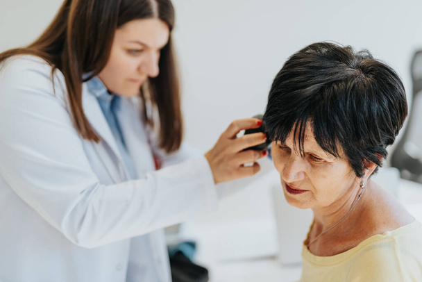 Oudere vrouw met oor video otoscopie onderzoeken in het moderne medische kantoor. Vakkundige en ervaren arts controleert haar oudere patiëntenoren. - Foto, afbeelding