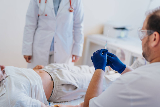 Un médico examina a un paciente que recibe terapia de perfusión en una habitación de hospital. Se proporciona atención médica y diagnóstico para una enfermedad. - Foto, Imagen