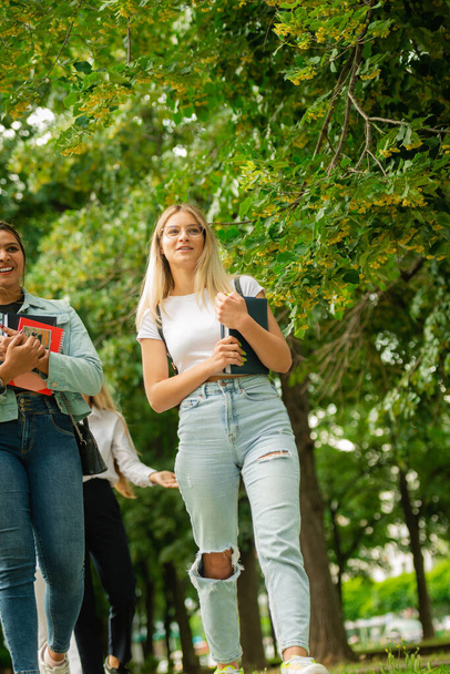 Foto de bajo ángulo de una pareja de estudiantes de secundaria o universitarios hablando y caminando juntos fuera de la escuela con mochilas y libros en sus manos - Foto, imagen