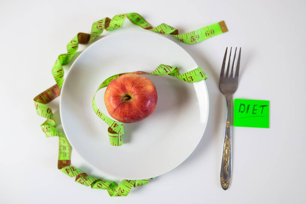 красное яблоко и мерная лента на тарелке как символ здорового питания. - Фото, изображение