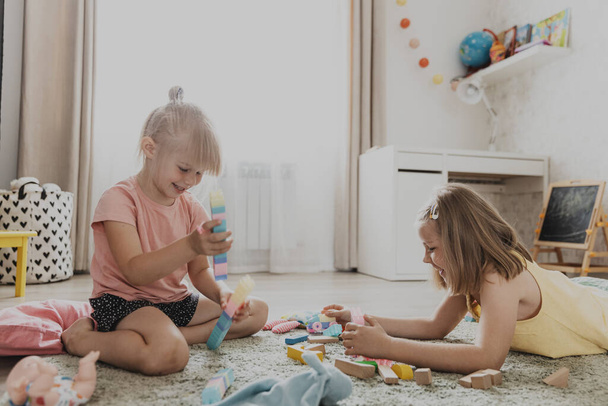 Дети играют с красочными игрушками. Дети, сидящие на ковре в домашней спальне или детском саду. Образовательная экологическая игра для ребенка. Милые сестрички строят дом, башню, веселятся - Фото, изображение