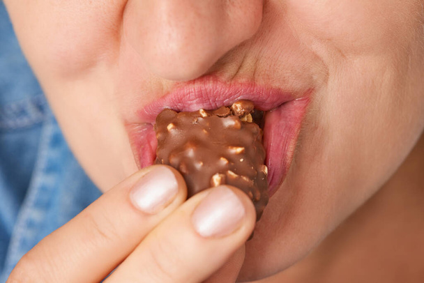 Primo piano di bocca di felice donna caucasica mangiare barretta di cioccolato con noci. Vista frontale. Vista ad angolo basso. - Foto, immagini