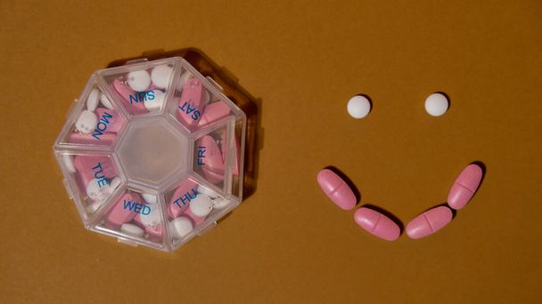 Szervező heti felvételek mosollyal készült tabletta napi vegye gyógyszert fehér rózsaszín gyógyszerek és kapszulák. Napi vitaminok otthon. Gyógyszer étrend-kiegészítők, immunitás és betegségmegelőzés - Fotó, kép