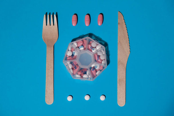Organizer wekelijkse shots met vork en mes medische pil doos met doses tabletten voor dagelijks innemen van medicijnen met witte roze drugs en capsules. Dagelijkse vitaminen thuis. Geneesmiddelen dieetsupplementen - Foto, afbeelding