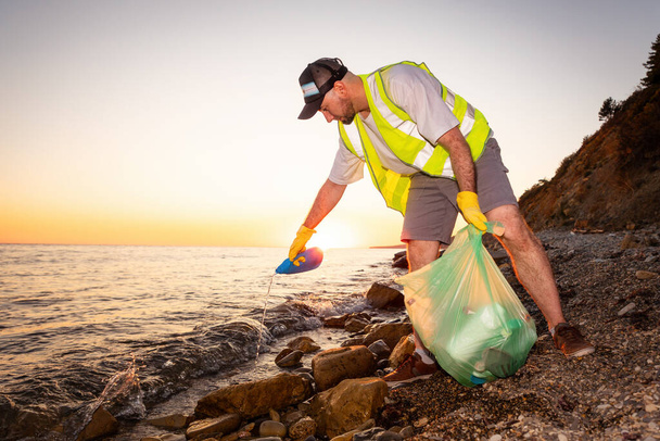 Pohled na dobrovolníka bělocha v vestě a gumových rukavicích, jak sbírá odpadky. Pojem znečištění oceánu. - Fotografie, Obrázek