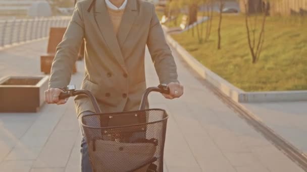 Tracking crop shot of unrecognizable woman wearing smart casual clothes riding bicycle in morning - Footage, Video