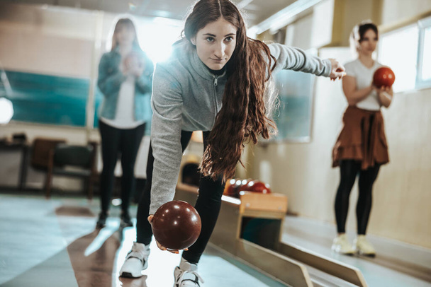 A cute girl throwing the bowling ball while her friends are standing in the back. - Photo, Image