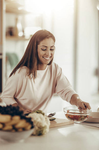 Aufnahme einer jungen lächelnden Frau, die in ihrer Küche eine gesunde Mahlzeit zubereitet. - Foto, Bild