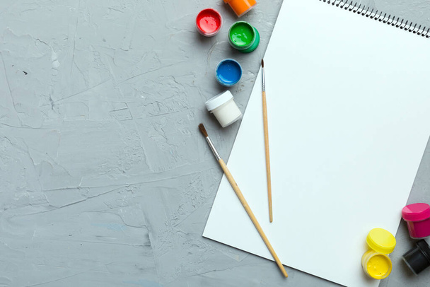 Albumseiten und Farben, Bleistifte, Pinsel auf farbigem Hintergrund. Draufsicht mit Leerraum. Arbeitsplatz für Kreativität. Konzeptzeichnung für den Heimunterricht. - Foto, Bild